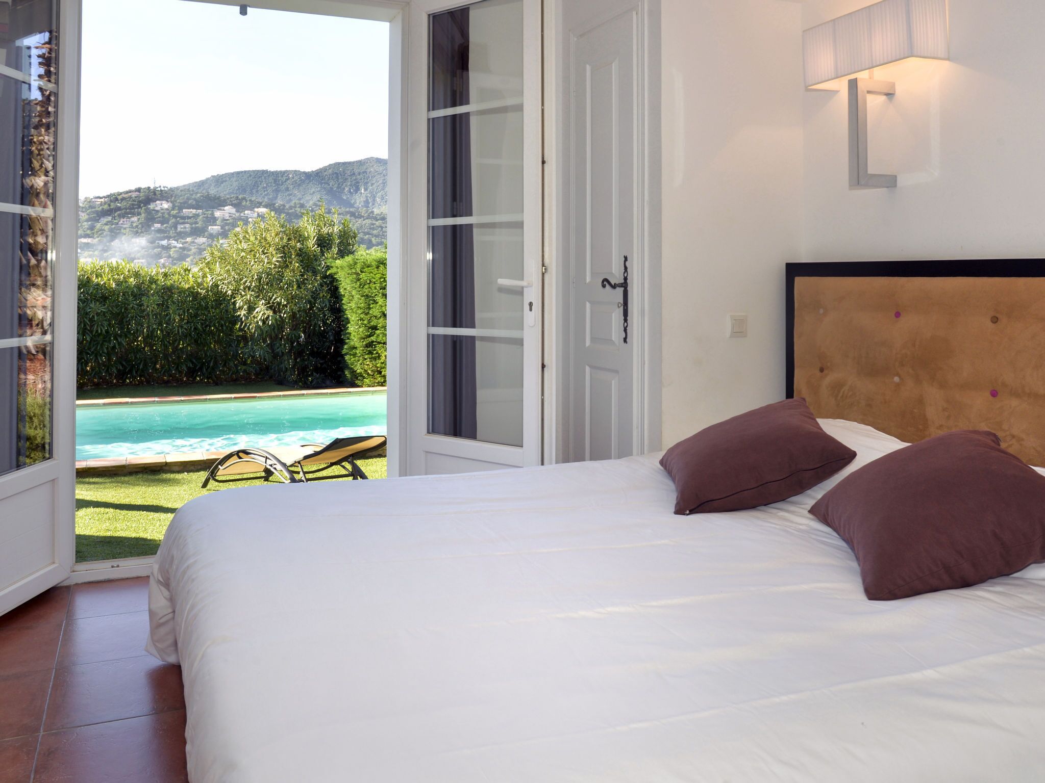 A bedroom with a bed, pillows, a view of a swimming pool, and a door leading outside.