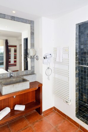 A bathroom with a stone sink, wooden vanity, a mirror, a towel rack, and a shower area with a tiled wall. - Domaine de l'Eilen V68I by Interhome (Cavalaire)
