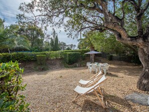 Une terrasse avec deux chaises longues et une table, entourée d’une zone recouverte de gravier et d’arbres.