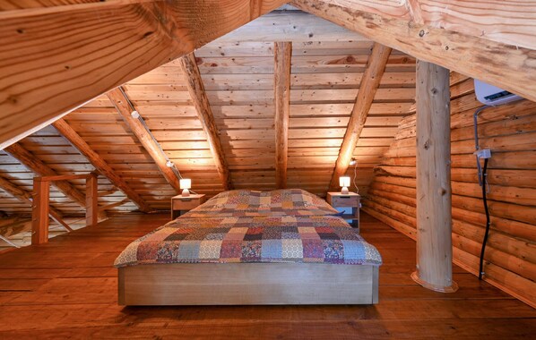 A cozy attic bedroom with a wooden floor, a quilted bedspread, and two bedside lamps.
