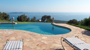 Une piscine aux bords recouverts de pierres, deux chaises longues et une vue sur la mer.