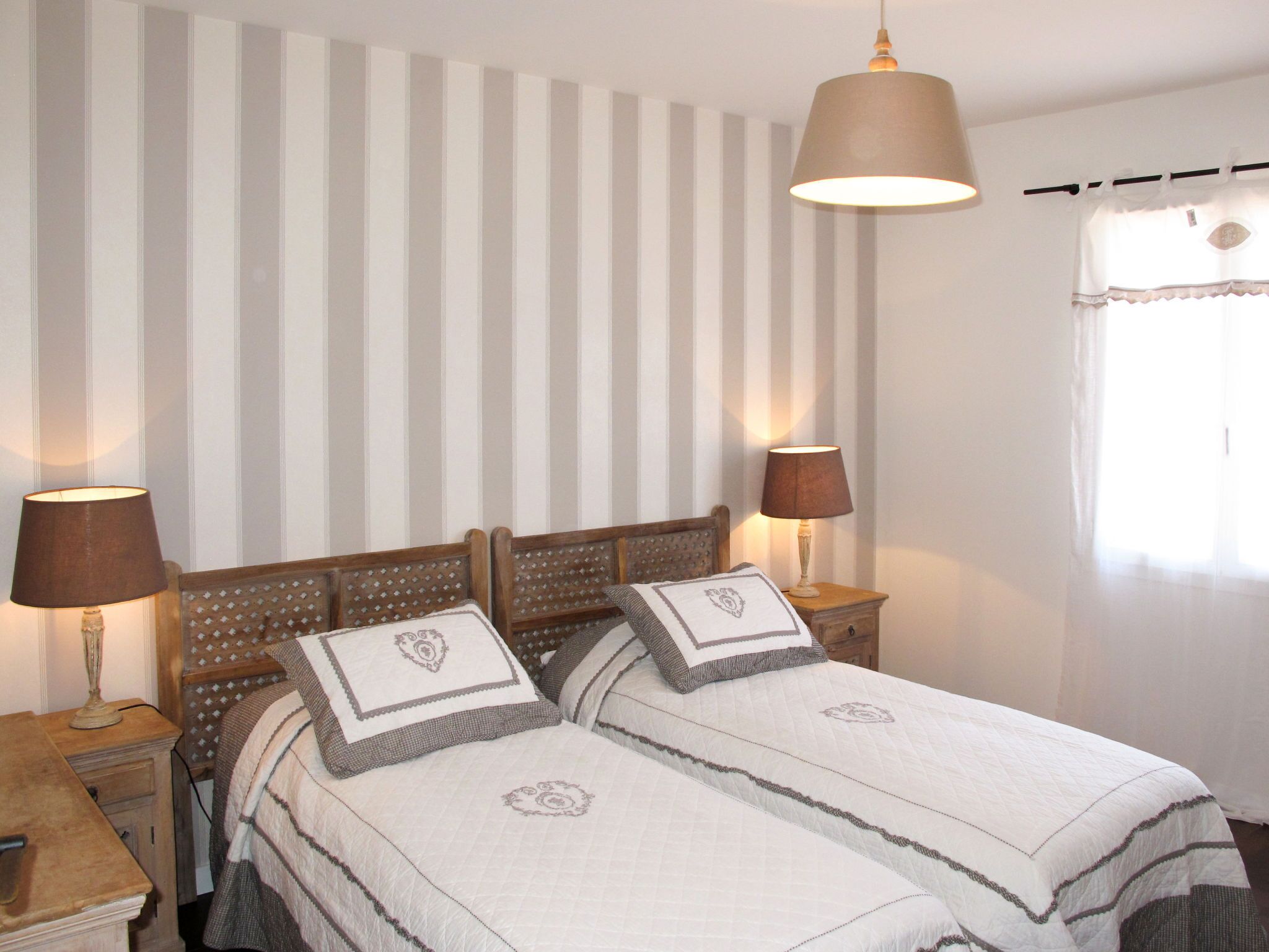 A double bed with a striped headboard, two bedside lamps, and a window with curtains.