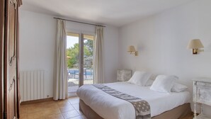Une chambre à coucher comprenant un lit, une table de chevet, une lampe et donnant sur un espace extérieur avec une piscine.