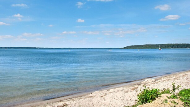 A beach with clear water, a sandy shore, and a distant forested landmass. - Lenzer Höh by Interhome (Plau am See)
