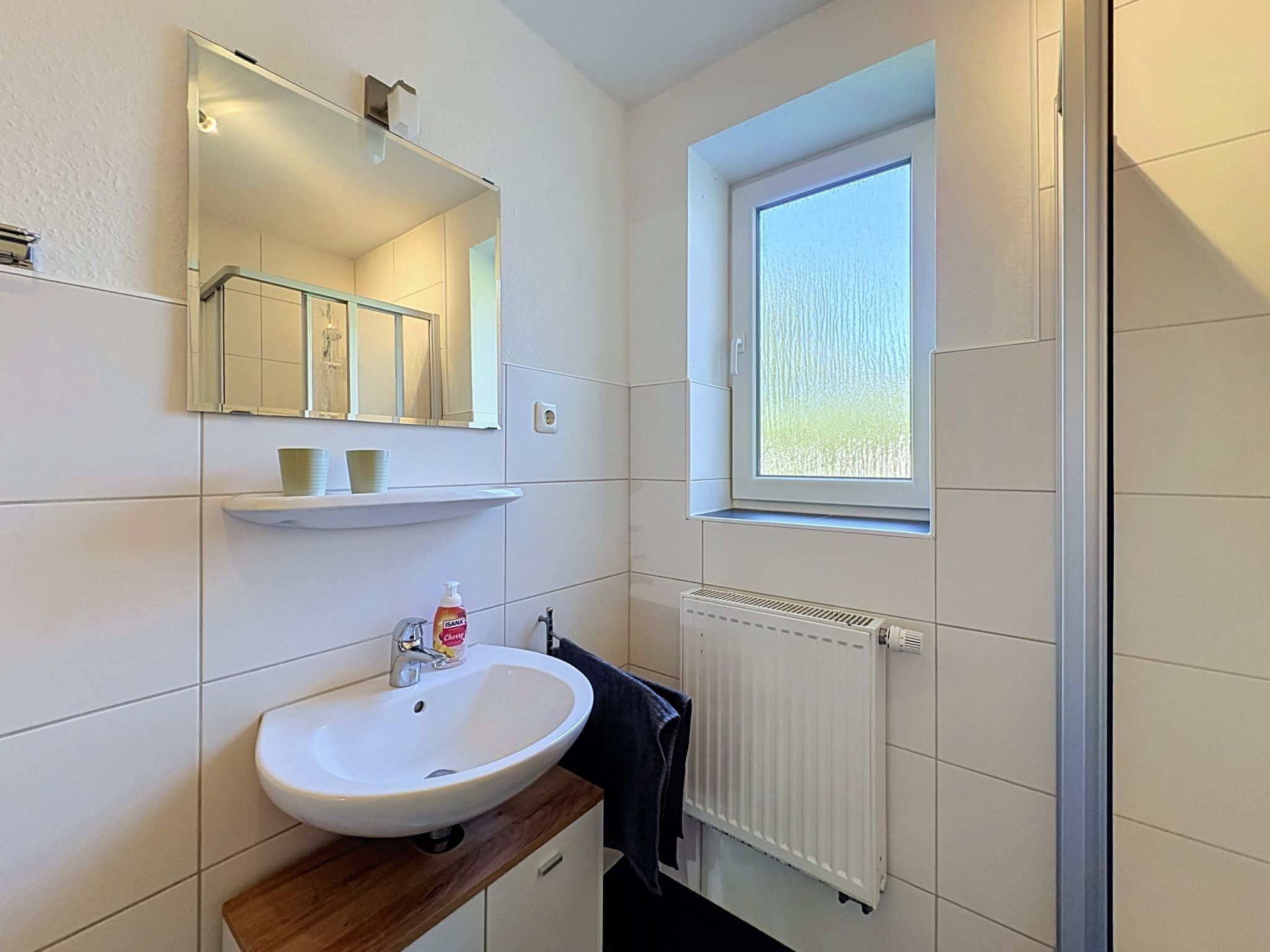 Une salle de bain avec un lavabo blanc, un miroir et une fenêtre.