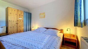 A bedroom with a bed, wooden wardrobe, curtains, a wall-mounted light, and a radiator. - Lenzer Höh by Interhome (Plau am See)