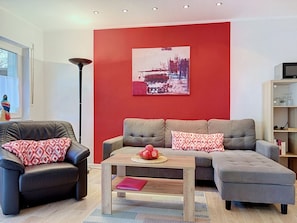 A modern living room with a red accent wall, a black leather sofa, a grey sectional, and a coffee table with apples. - Lenzer Höh by Interhome (Plau am See)