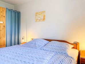 A double bed with a patterned bedspread, a wooden wardrobe, and a wall-mounted artwork. - Lenzer Höh by Interhome (Plau am See)