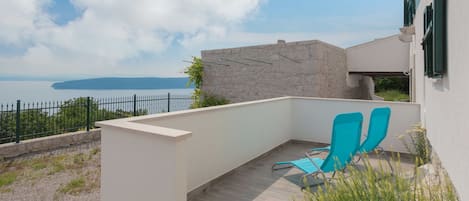A balcony with two blue chairs, a stone wall, and a view of the sea.
