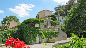 Un bâtiment traditionnel en pierre, doté d’un toit en pente, entouré d’une végétation luxuriante et de plantes à fleurs.