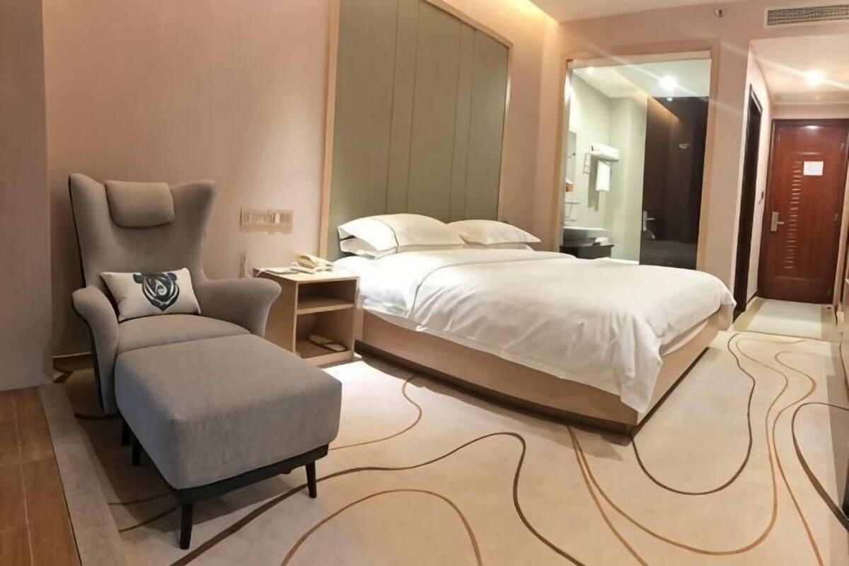 Ein Hotelzimmer mit Bett, Sessel, Nachttisch und großem Spiegel.