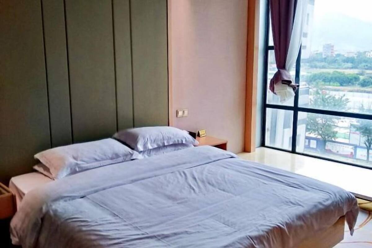 Ein Schlafzimmer mit Bett, Nachttisch und Fenster mit Blick auf die Stadt.