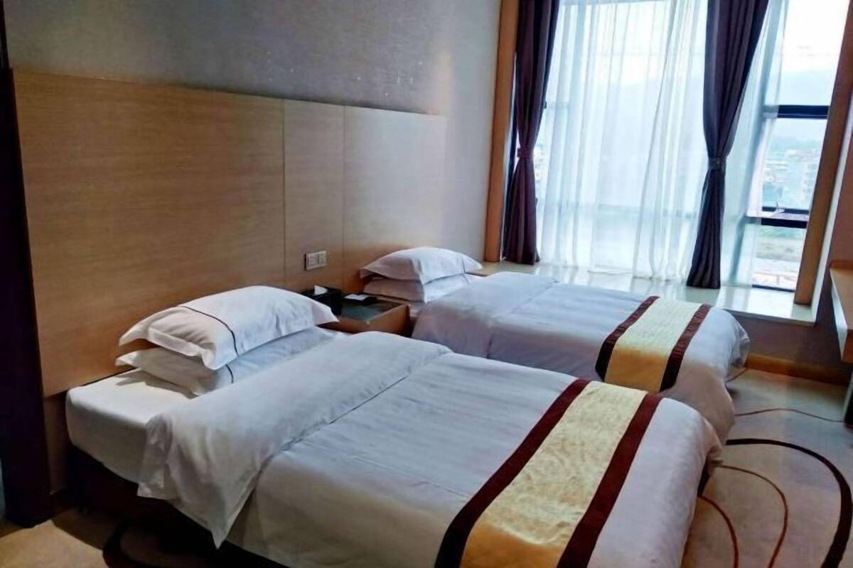 Ein Hotelzimmer mit zwei Betten, einem großen Fenster mit Vorhängen und Blick auf die Stadt.