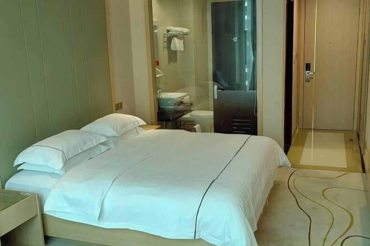 Ein Hotelzimmer mit einem großen Bett, einem Nachttisch, einem Spiegel, einer Tür und einem Duschbereich.