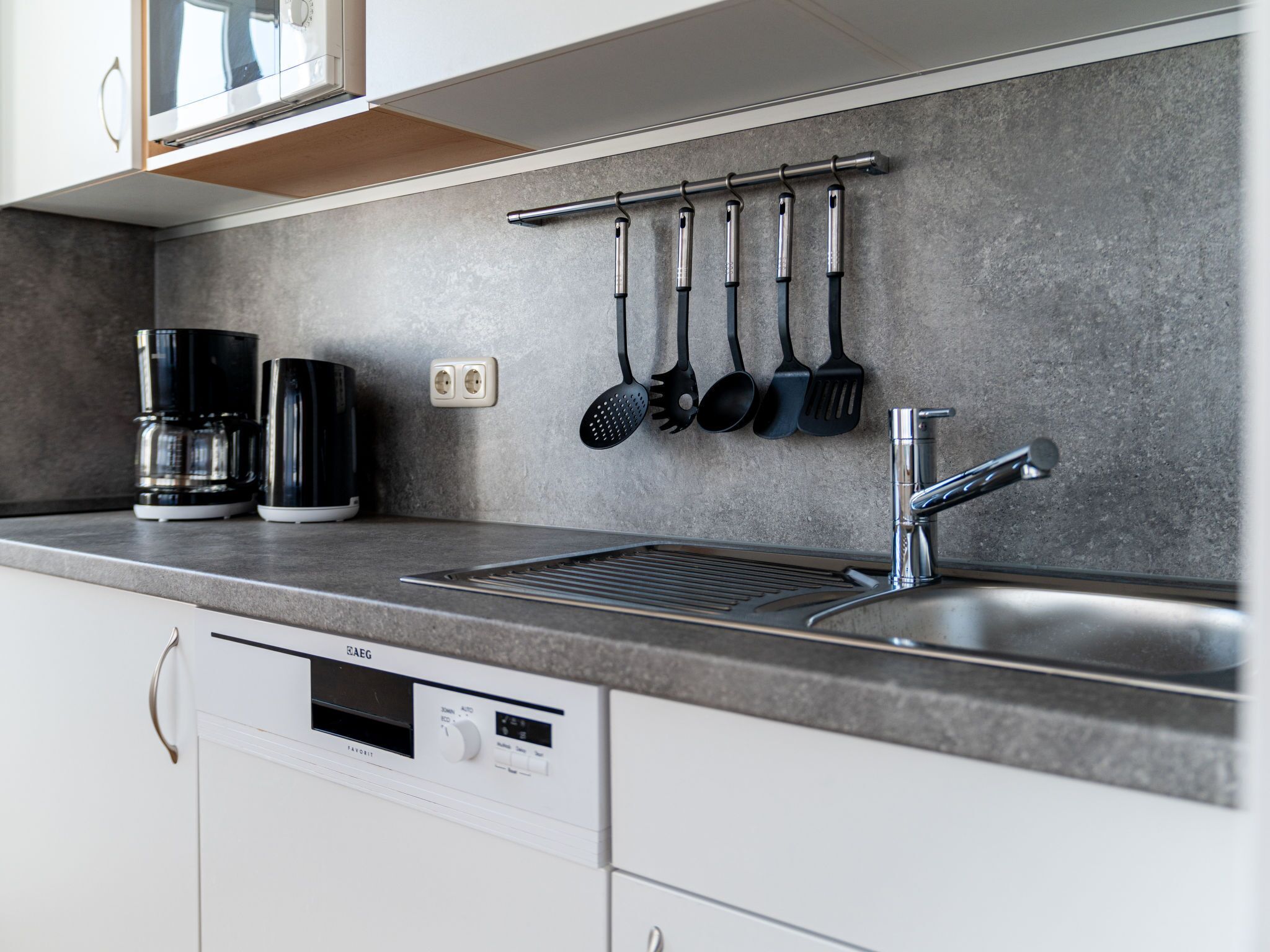A modern kitchen with a built-in dishwasher, a coffee maker, and a stainless steel sink.