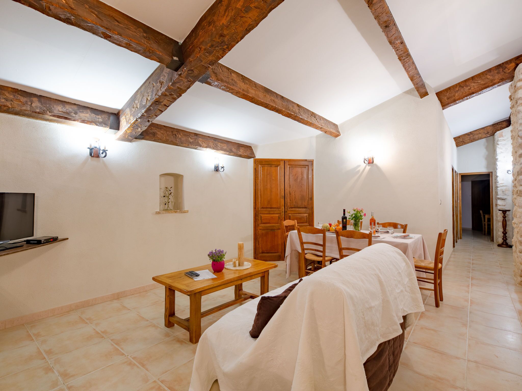 A dining area with wooden beams, a TV, and a table set for two.