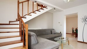 Una sala de estar moderna con un sofá seccional gris, una mesa de centro de vidrio y una escalera de madera.