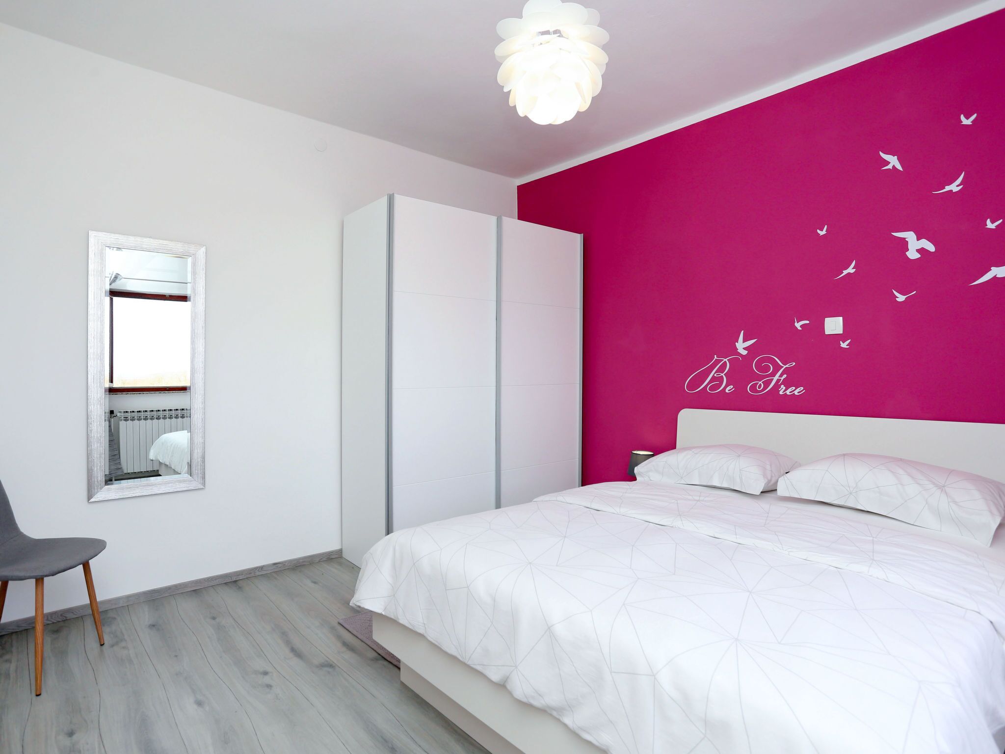 Une chambre moderne avec un lit, une armoire, un miroir et un mur orné d’un autocollant avec l’inscription « Soyez libre ».