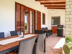 Enjoy meals in this dining area with a long table and wicker chairs, surrounded by a stone wall and wooden beams.