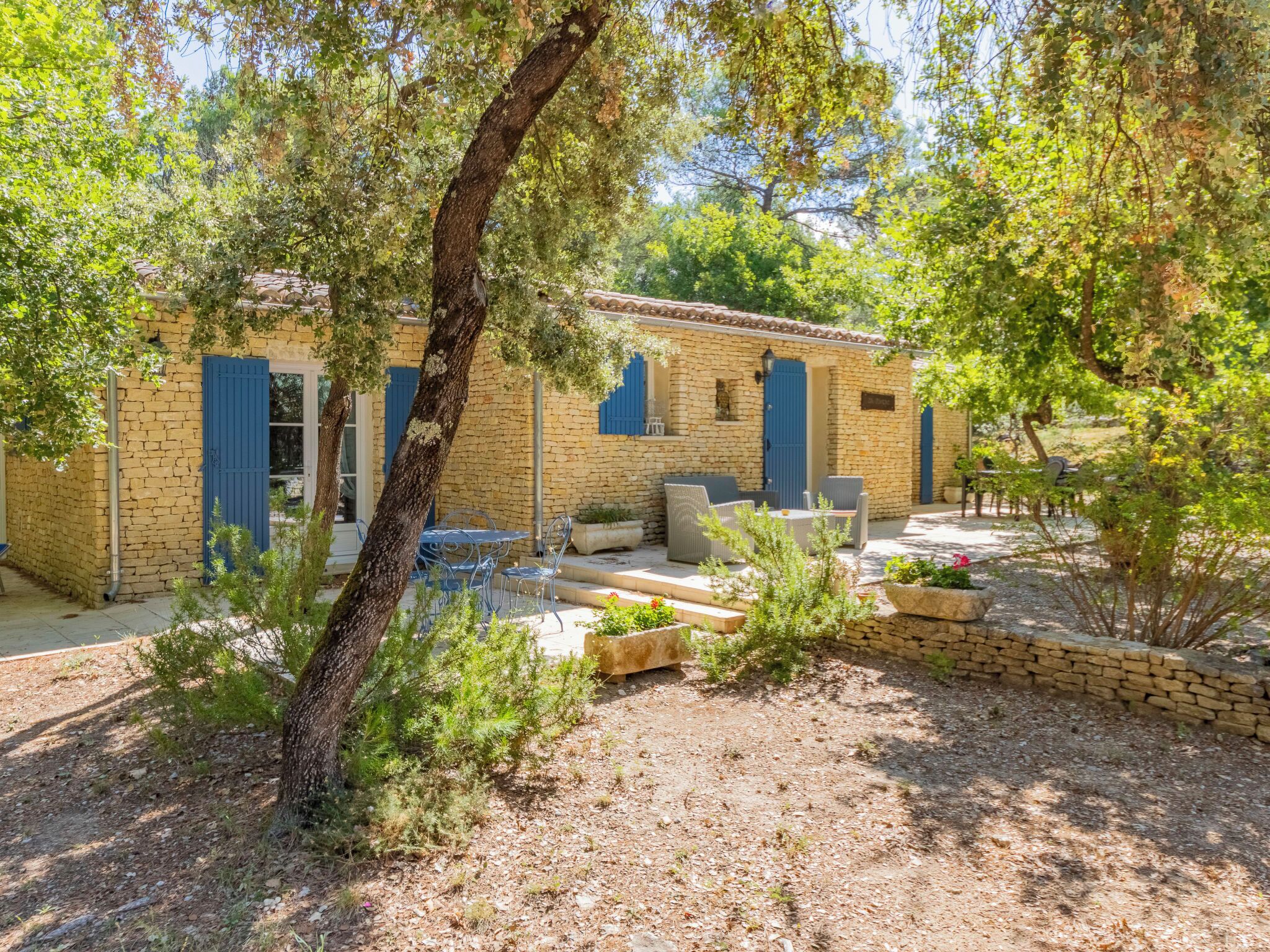 A stone building with blue shutters, outdoor seating, and a garden area.