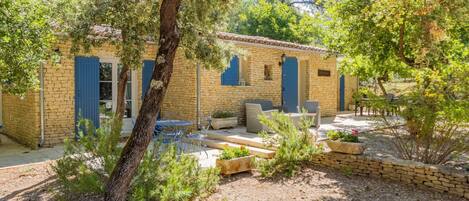 A stone building with blue shutters, outdoor seating, and a garden area.