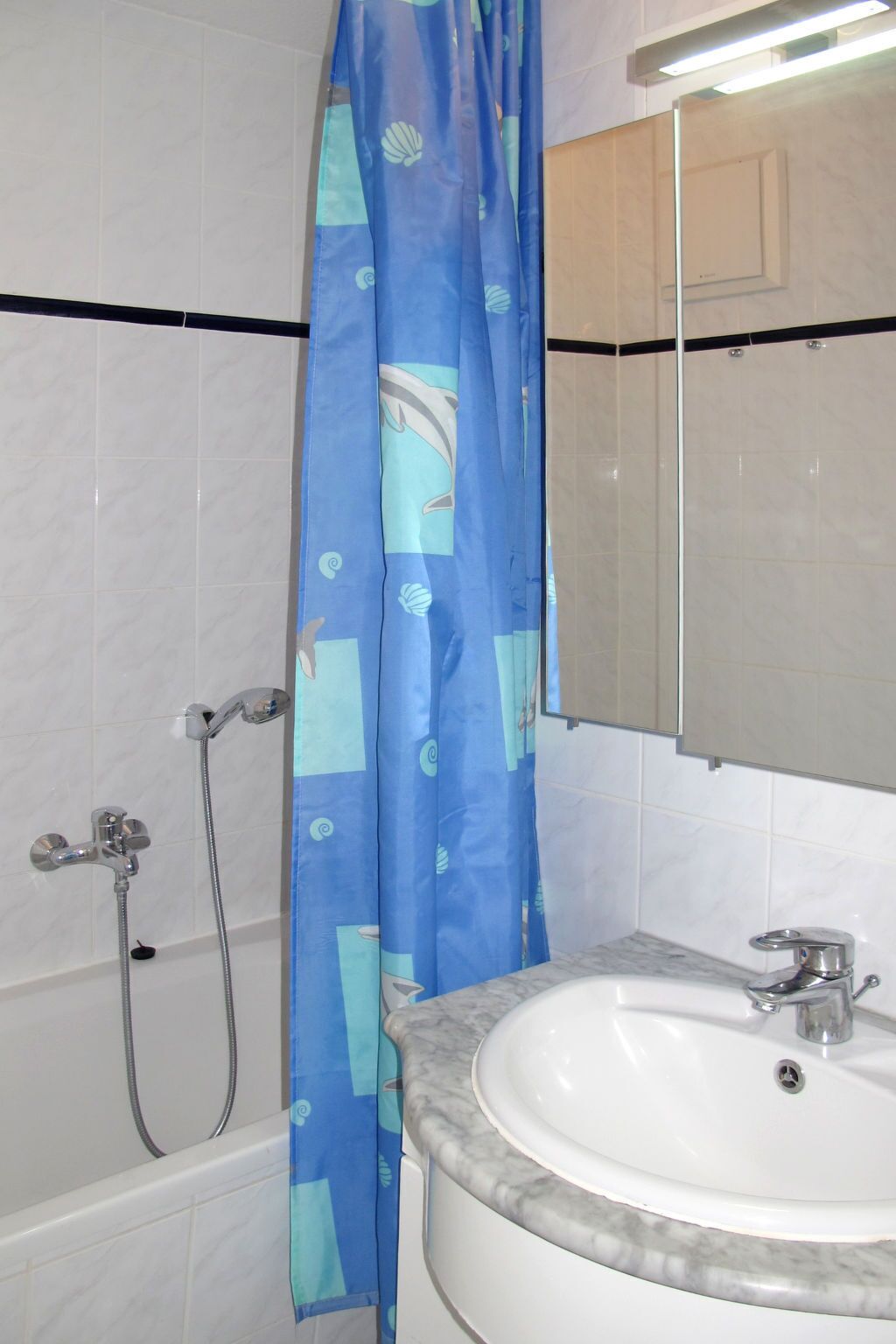 Une salle de bain avec un lavabo blanc, un miroir, une douche avec un rideau de douche bleu et une baignoire.