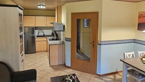 Eine kleine Küche mit Kühlschrank, Spüle und Mikrowelle. Es gibt einen Essbereich mit Tisch und Stühlen.
