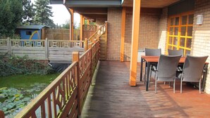 Eine überdachte Terrasse im Freien mit Holzdeck, Backsteinwand und Tisch mit Stühlen.