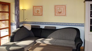 Ein Wohnzimmer mit einer Eckcouch, einem kleinen Tisch und zwei gerahmten Bildern an der Wand.