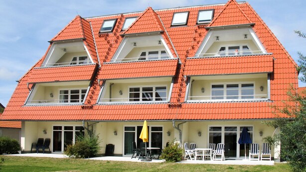 A two-story building with a red-tiled roof, multiple windows, and a front patio with outdoor seating. - Kap Arkona by Interhome (Breege)