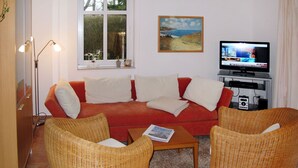 A living room with a red sofa, two wicker chairs, a coffee table, a television, and a painting on the wall. - Kap Arkona by Interhome (Breege)
