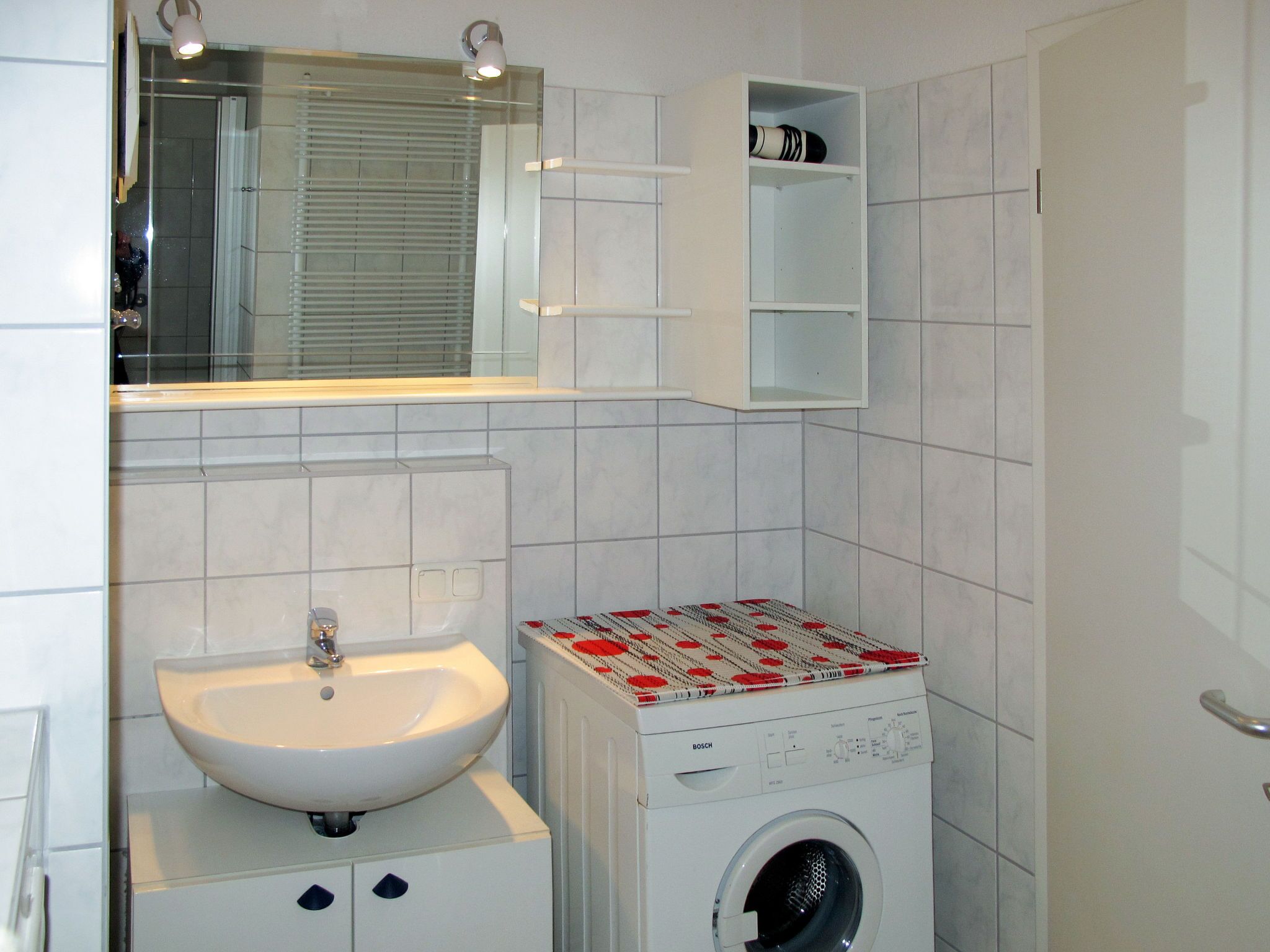 A compact bathroom with a white sink, a Bosch washing machine, and a mirror above the sink.