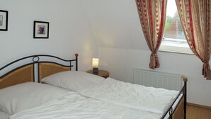 Una cama individual con cabecera de madera, una mesita de noche con lámpara y una ventana con cortinas estampadas.