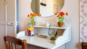 Un meuble-lavabo de salle de bain avec un miroir, deux pots de fleurs, un bocal en verre contenant des fleurs et une sculpture d’oiseau décorative.