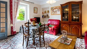 Un coin repas avec une table dressée pour quatre personnes, un canapé rouge, un meuble en bois avec des portes en verre et un sol à motifs.