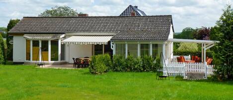 A house with a large garden, a covered patio, and a white picket fence.