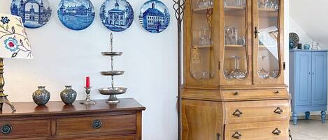 A wooden cabinet with glass doors, a wooden dresser with drawers, and a wall with blue decorative plates.