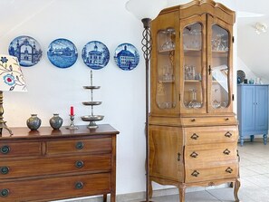 Un meuble en bois avec des portes en verre, une commode en bois avec des tiroirs et un mur décoré d’assiettes bleues.