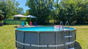 Ein überirdischer Pool mit einer Leiter, umgeben von einem Rasen und Bäumen.
