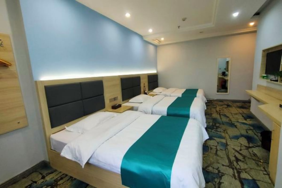 Habitación de hotel con dos camas, cabecero de madera, mesita de noche, espejo y alfombra estampada.