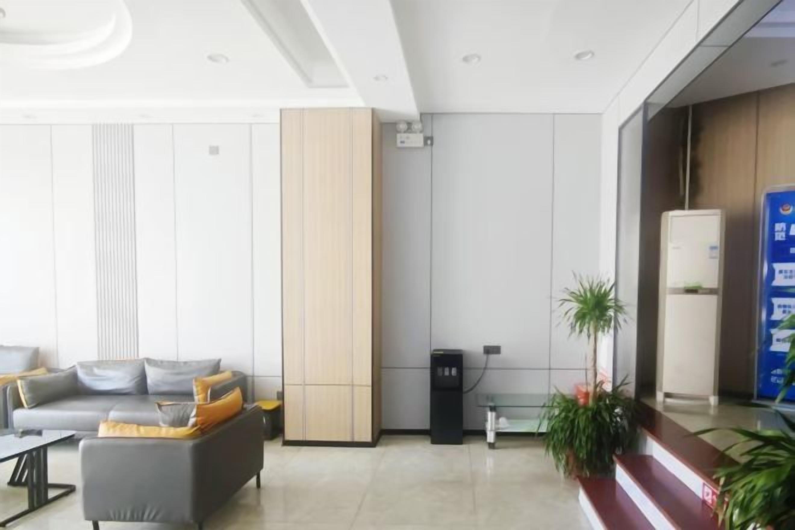A modern lobby with a sofa, a tall cabinet, a refrigerator, and a plant.