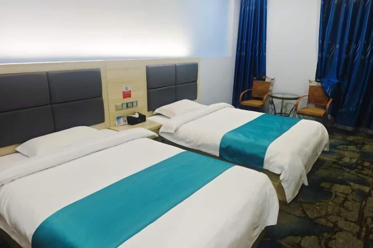Une chambre d’hôtel avec deux lits, une petite table, deux chaises et une fenêtre avec des rideaux.