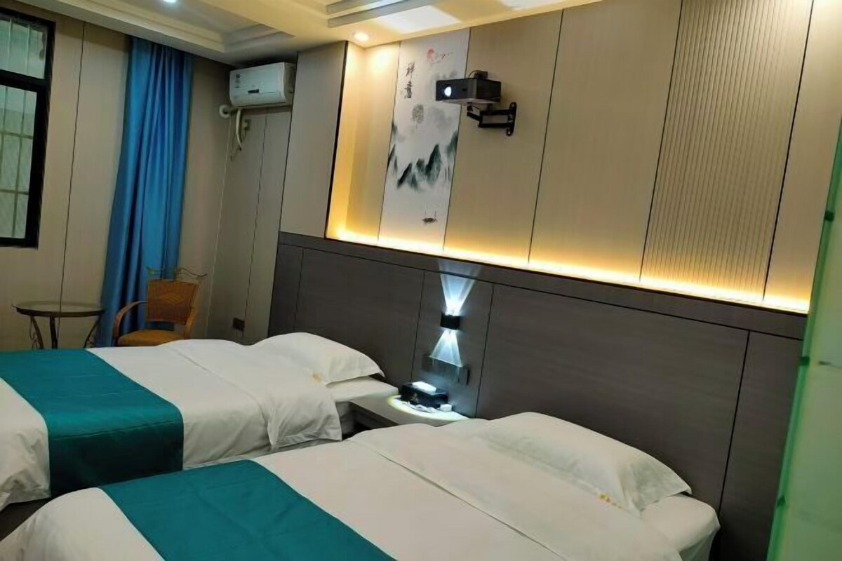 Hotelkamer met twee bedden, een bureau met lamp, een wandairconditioner en een kleine tafel met stoel.