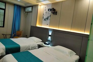 Hotelkamer met twee bedden, een bureau met lamp, een wandairconditioner en een kleine tafel met stoel.