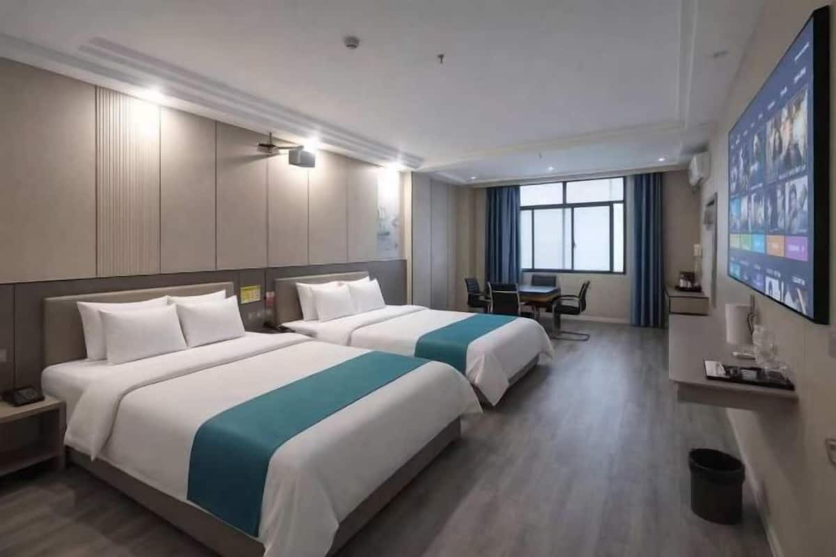 Une chambre d’hôtel avec deux lits, un bureau, une chaise et un grand écran de télévision.