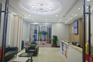 Zona de recepción de hotel con mostrador, área de descanso y un espejo grande que refleja el interior.