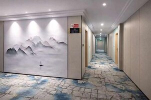 Pasillo de hotel con alfombra estampada, un mural en la pared con montañas y puertas que dan a las habitaciones.