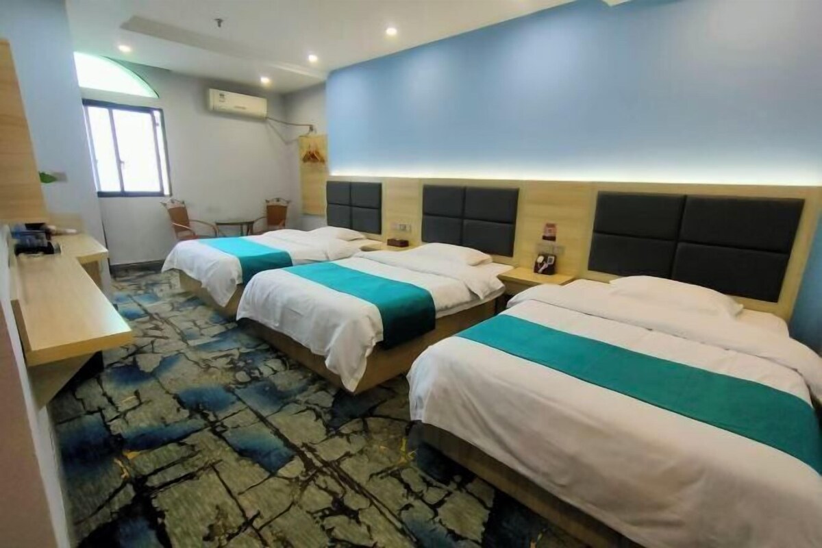 Een hotelkamer met drie bedden, een bureau, een stoel en een raam.