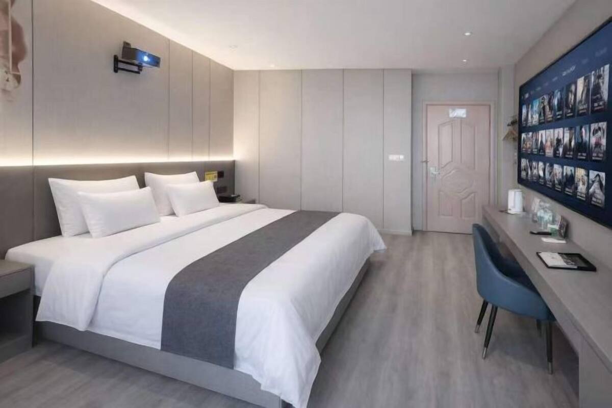 Une chambre d’hôtel moderne dotée d’un grand lit, d’un bureau et d’un présentoir photo fixé au mur.