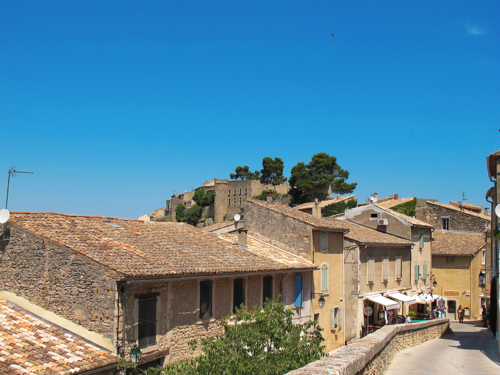 A historic town with stone buildings, narrow streets, and a prominent hill with trees.